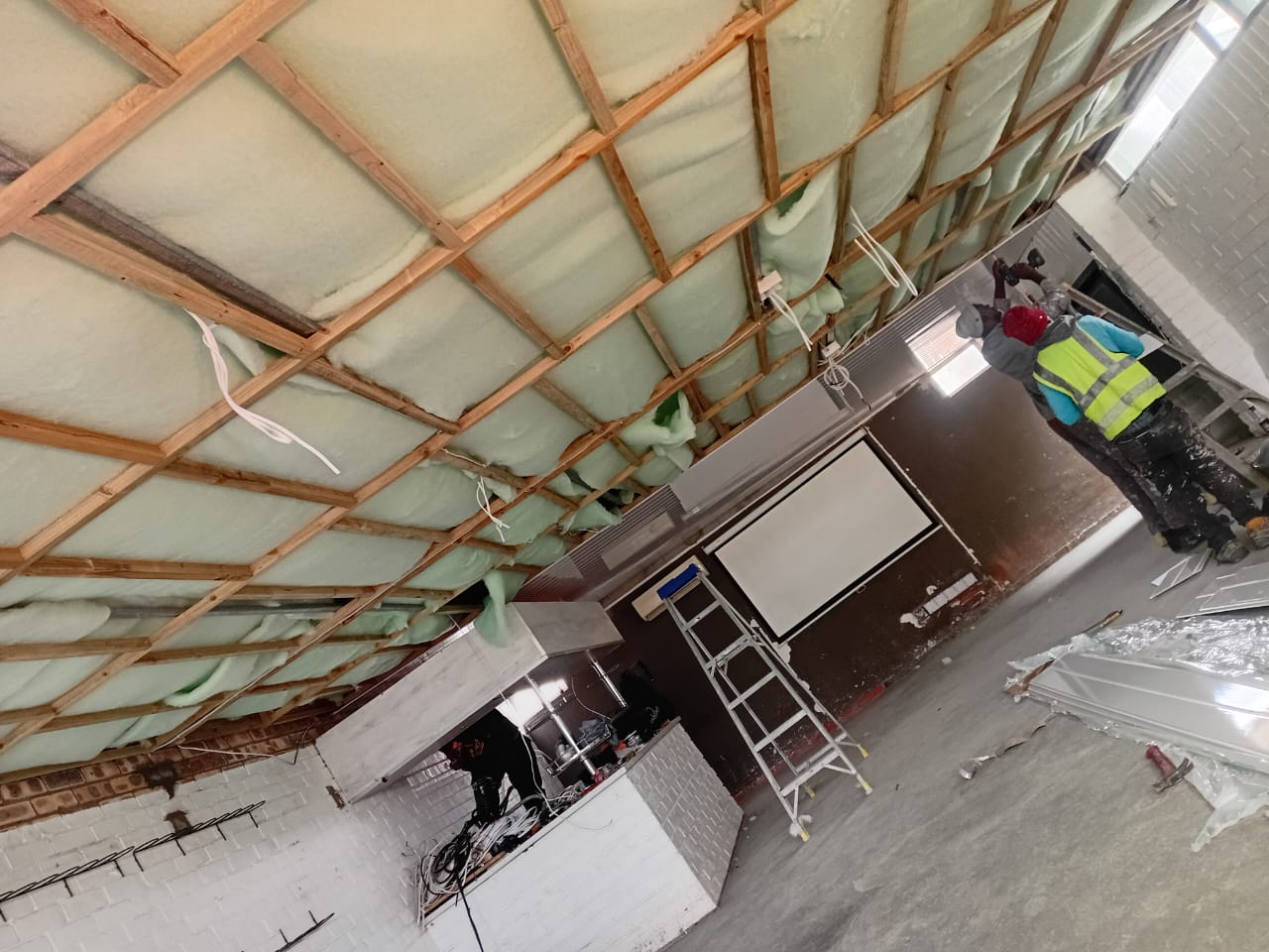 Before: Commercial interior with exposed timber ceiling battens, roof insulation, electrical wiring and unfinished feature wall area